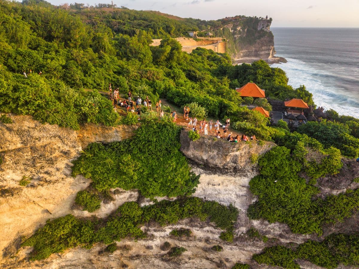 Uluwatu cliff temple from above, ancient Hindu shrine perched 70 meters over the Indian Ocean, visitors gathering for sunset and Kecak