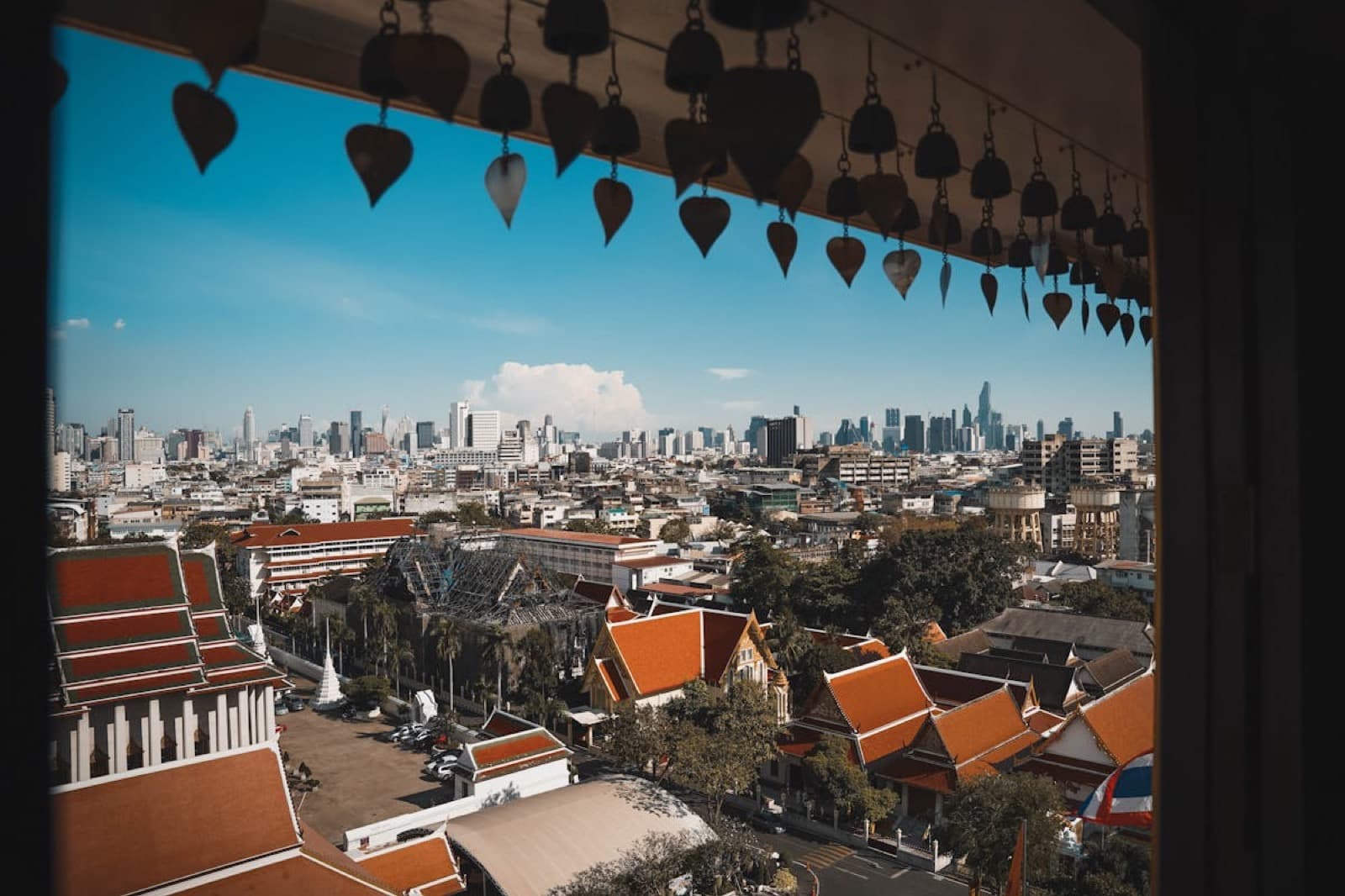 Bangkok skyline from Wat Pho temple tower, red-tiled temple roofs in the foreground, modern glass towers rising behind