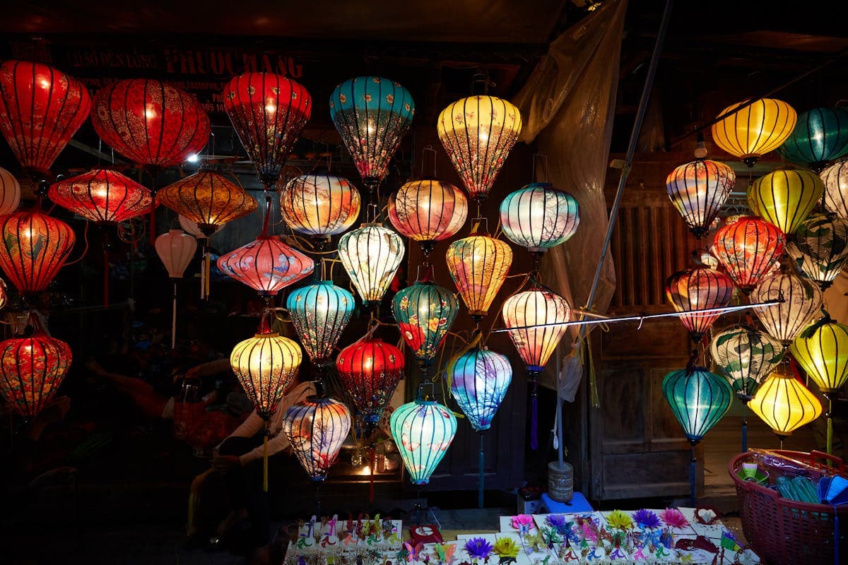 Hoi An lantern shop at night, colorful silk lanterns packed ceiling to floor, glowing in red, yellow, teal, and blue. The streets glow like this every evening after sunset.