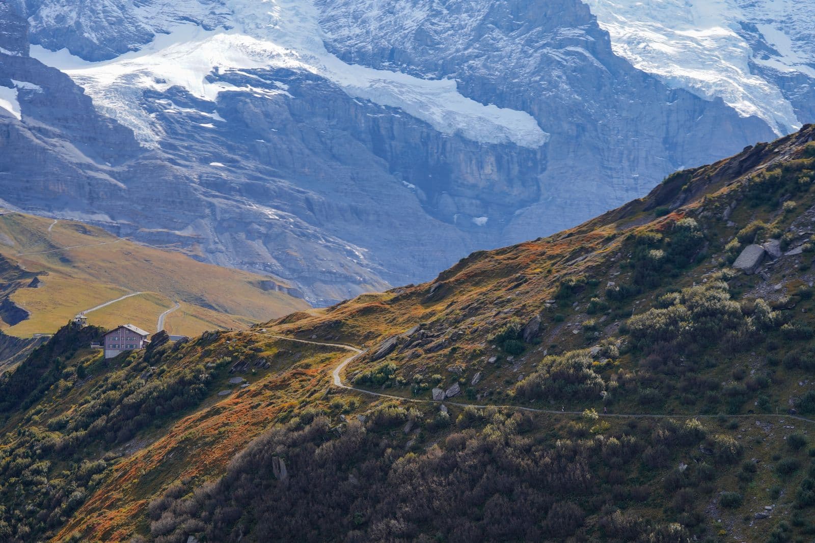 An autumn hiking path and mountain hut below the glacier walls of the Jungfrau massif