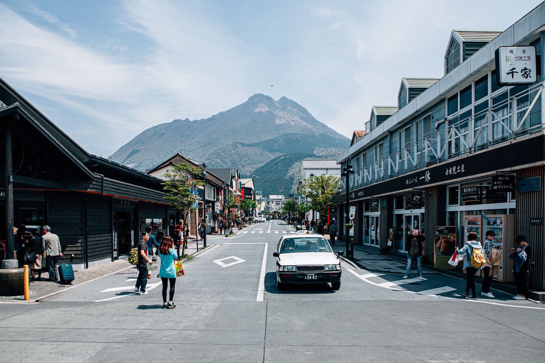 Yunotsubo shopping street in Yufuin with Mount Yufu rising behind the shopfronts and visitors walking