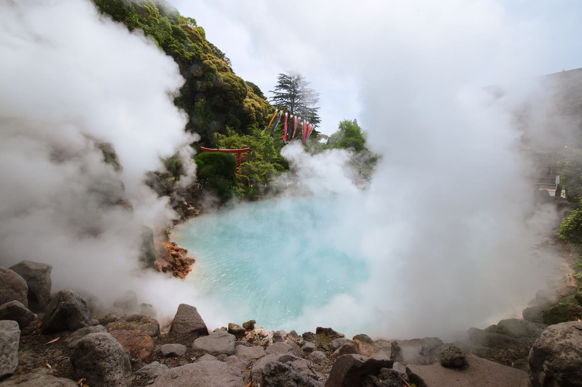 Cobalt blue hot spring pool at Beppu's Umi Jigoku with steam rising and a red torii gate behind
