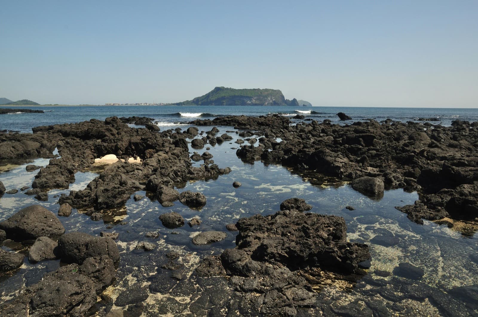 Jeju's volcanic coastline near Seongsan, black basalt lava rock meets clear blue water