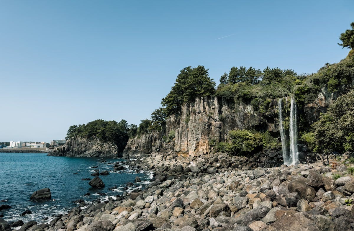 Jeju coastal waterfall, basalt cliff face with waterfall dropping directly into the sea