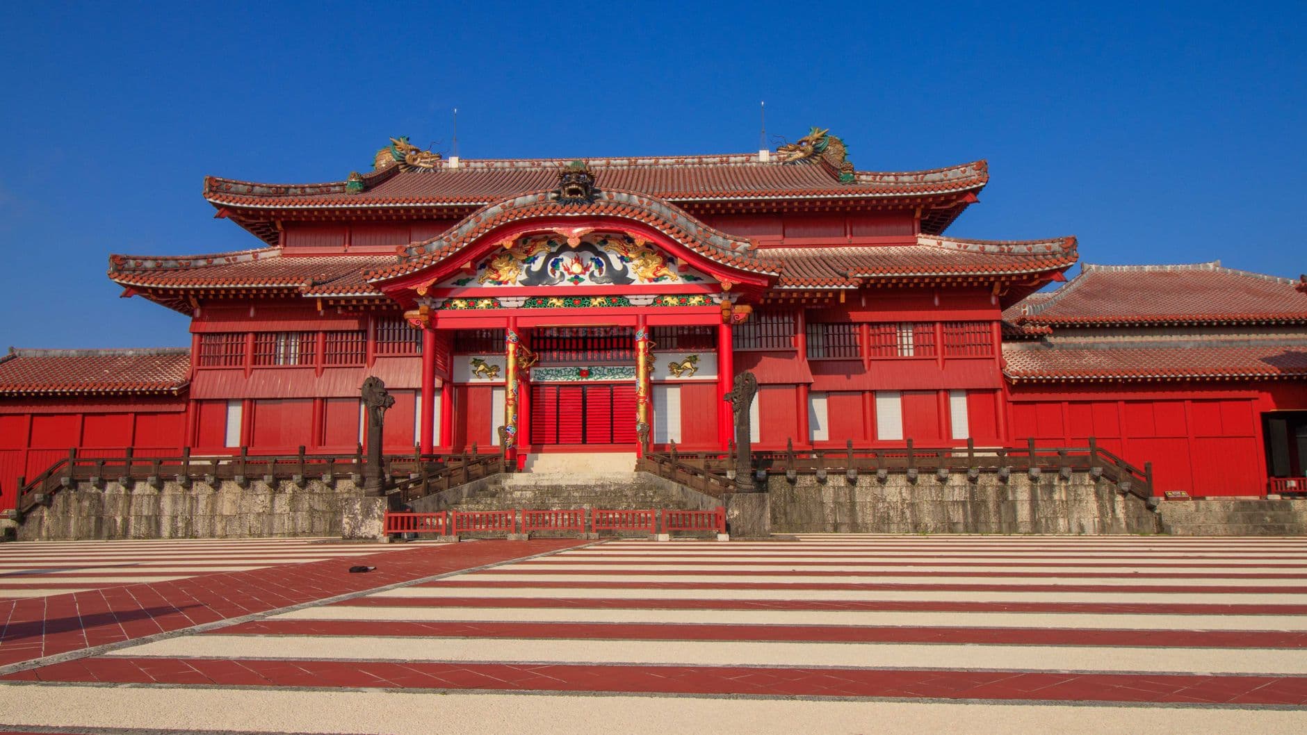 Front view of the Shuri Castle main hall with red roof tiles and the striped Una plaza