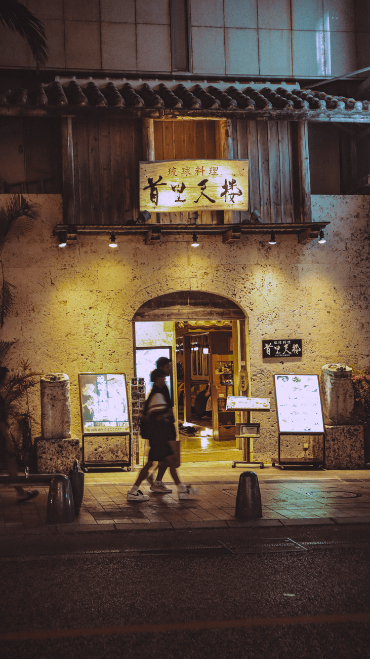 Stone facade and lit entrance of a Ryukyu cuisine restaurant on Kokusai Street at night
