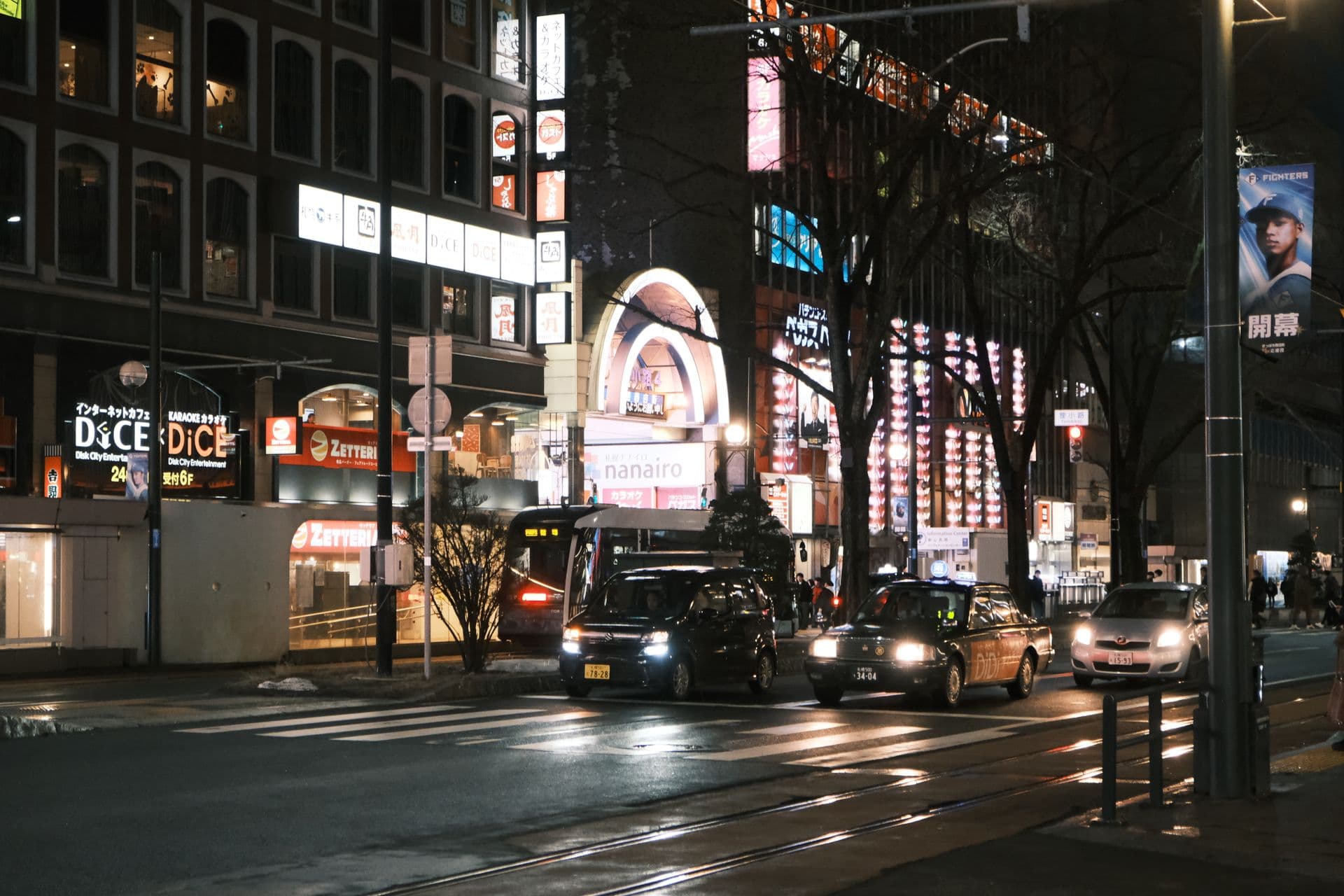 Neon-lit streetcar street at night near Susukino with the Tanukikoji arcade entrance